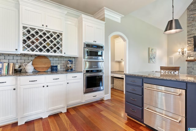 kitchen with decorative light fixtures, light stone counters, light wood-style floors, arched walkways, and white cabinets