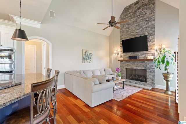 living area featuring arched walkways, a stone fireplace, visible vents, and dark wood-style flooring