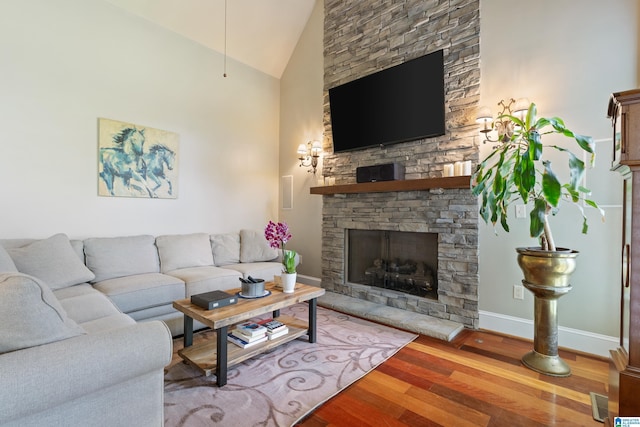 living room with a stone fireplace, wood finished floors, baseboards, and high vaulted ceiling