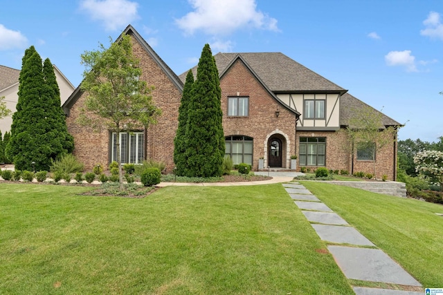 english style home with brick siding, a shingled roof, and a front lawn