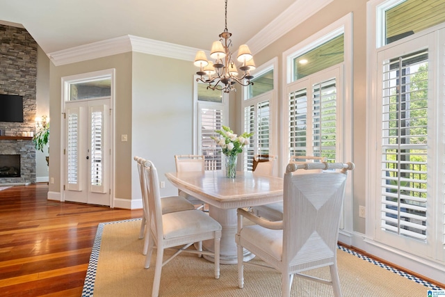 dining room featuring a stone fireplace, a notable chandelier, wood finished floors, and ornamental molding