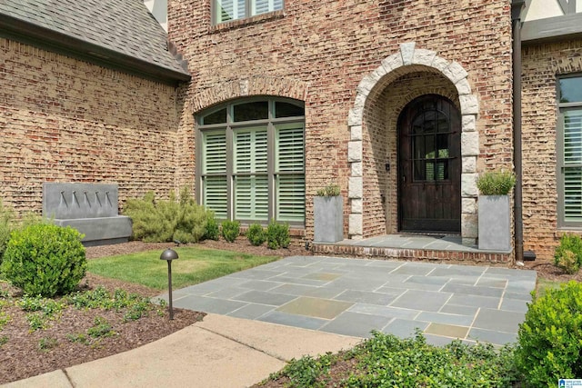 doorway to property with brick siding and a shingled roof