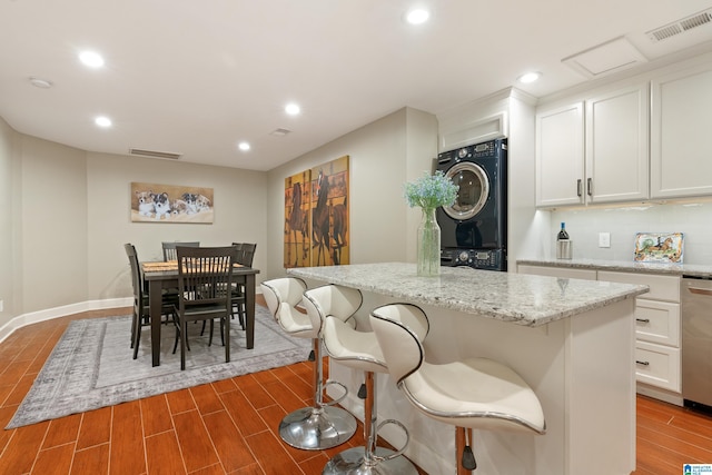 kitchen with wood finished floors, light stone countertops, stacked washer and dryer, white cabinetry, and tasteful backsplash