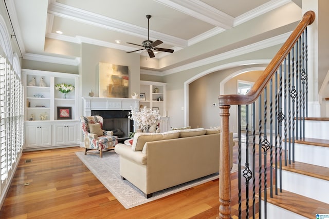 living room featuring built in shelves, stairway, arched walkways, light wood-style floors, and a fireplace