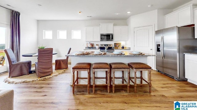 kitchen with stainless steel appliances, a kitchen island with sink, white cabinetry, and a breakfast bar area