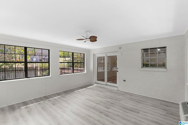 empty room featuring wood-type flooring, brick wall, and ceiling fan