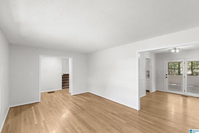 empty room with light wood-type flooring, a textured ceiling, and a chandelier