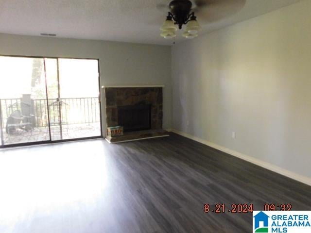 unfurnished living room featuring dark hardwood / wood-style flooring, a stone fireplace, and ceiling fan