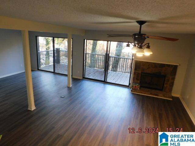 unfurnished living room with a fireplace with raised hearth, ceiling fan, a textured ceiling, baseboards, and dark wood finished floors