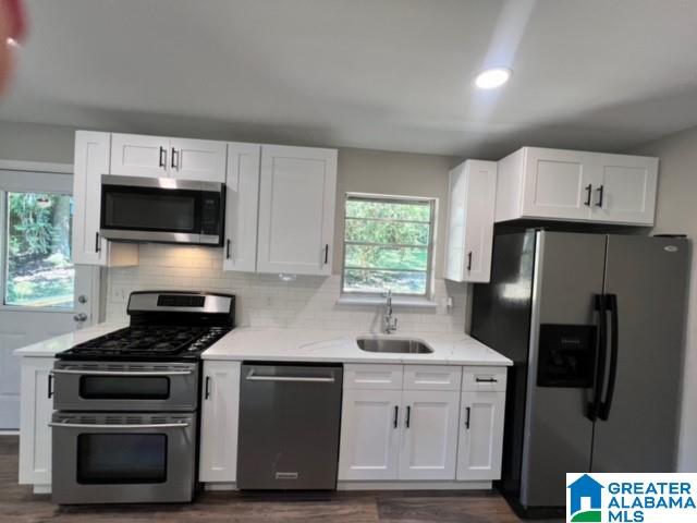 kitchen with white cabinets, appliances with stainless steel finishes, light stone counters, sink, and dark wood-type flooring