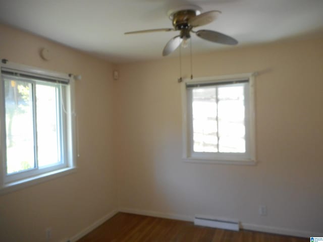 spare room featuring hardwood / wood-style floors, ceiling fan, a baseboard heating unit, and a healthy amount of sunlight