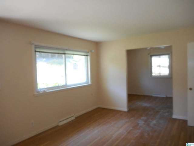 empty room with baseboard heating, plenty of natural light, wood finished floors, and baseboards