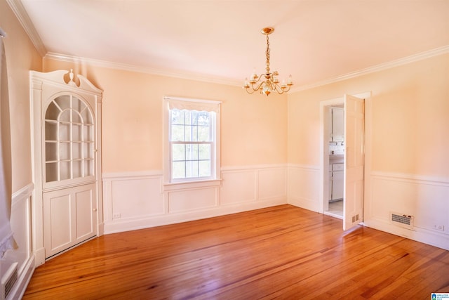 empty room with hardwood / wood-style floors, an inviting chandelier, and ornamental molding