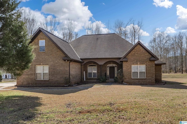 traditional-style home featuring a shingled roof, a front yard, and brick siding