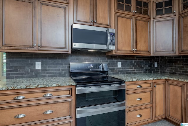 kitchen featuring light tile patterned floors, brown cabinetry, decorative backsplash, appliances with stainless steel finishes, and light stone countertops