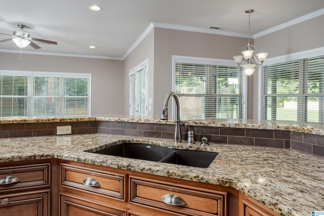 kitchen featuring light stone counters, brown cabinets, hanging light fixtures, crown molding, and a sink