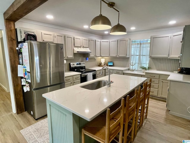 kitchen featuring pendant lighting, an island with sink, stainless steel appliances, sink, and light wood-type flooring