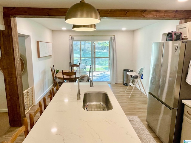 kitchen with stainless steel fridge, light stone countertops, beamed ceiling, and sink