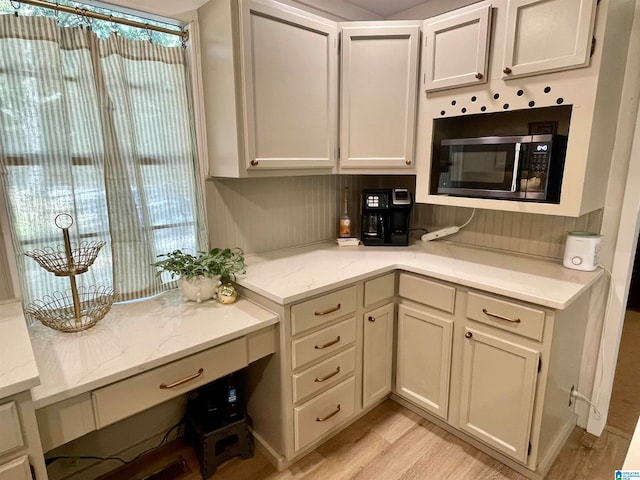 kitchen featuring light wood-type flooring, light stone countertops, and stainless steel microwave