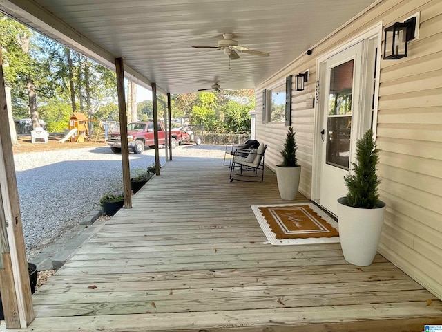 wooden terrace with a porch, ceiling fan, and a playground