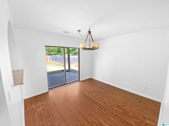 spare room featuring dark wood-type flooring and an inviting chandelier