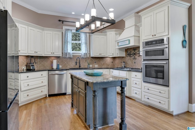 kitchen featuring a kitchen island, an inviting chandelier, appliances with stainless steel finishes, sink, and light wood-type flooring