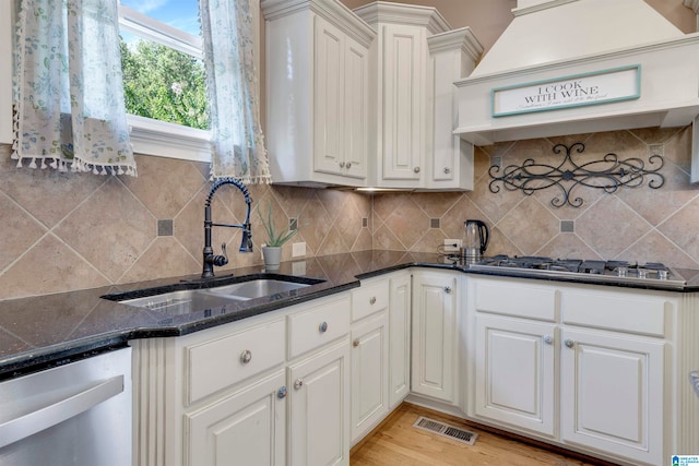 kitchen with white cabinets, dark stone countertops, light wood-type flooring, stainless steel appliances, and premium range hood