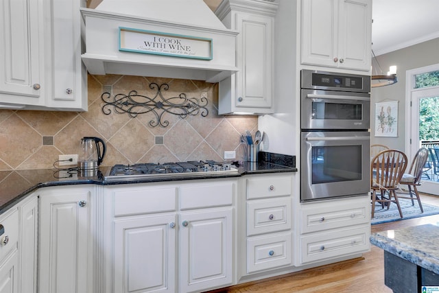 kitchen with white cabinetry, stainless steel appliances, an inviting chandelier, decorative backsplash, and custom range hood