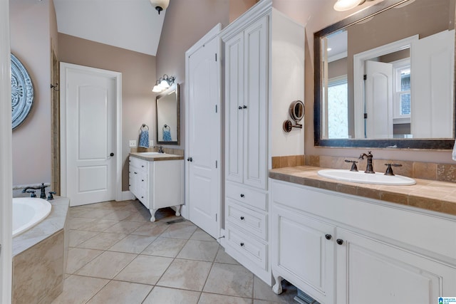 bathroom with tile patterned floors, vanity, tiled bath, and vaulted ceiling