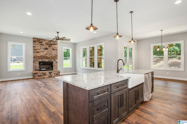 kitchen featuring a fireplace, decorative light fixtures, ceiling fan with notable chandelier, light stone counters, and dark wood-type flooring