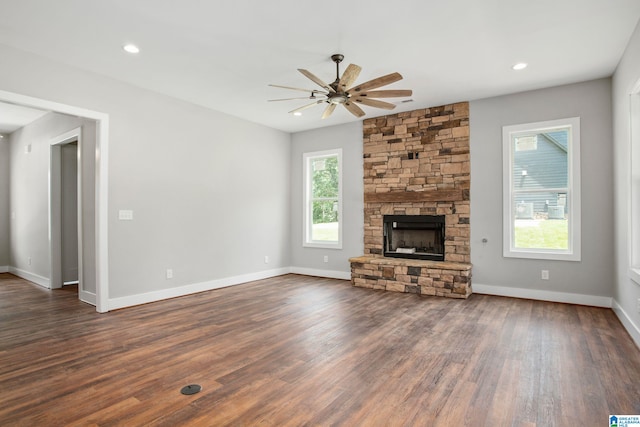 unfurnished living room featuring a healthy amount of sunlight, ceiling fan, dark hardwood / wood-style floors, and a stone fireplace