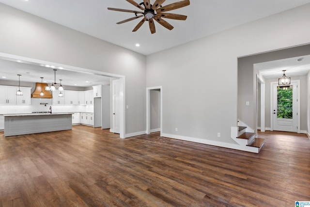 unfurnished living room featuring dark wood-style floors, recessed lighting, ceiling fan with notable chandelier, baseboards, and stairs