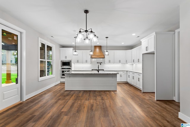 kitchen featuring appliances with stainless steel finishes, custom range hood, a center island with sink, and white cabinetry