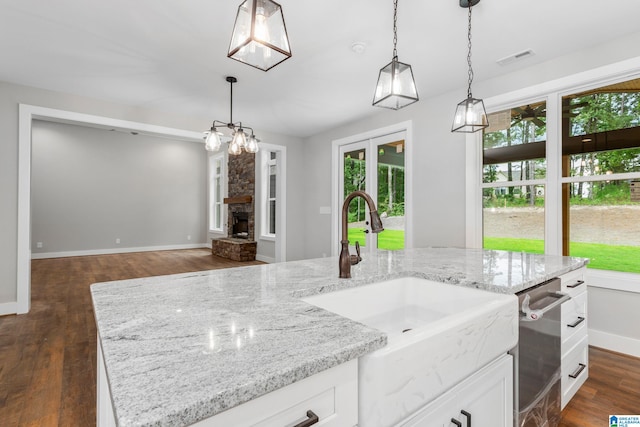 kitchen with light stone counters, dark wood-type flooring, white cabinetry, a center island with sink, and pendant lighting