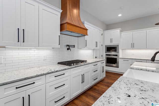 kitchen featuring dark wood-style flooring, custom exhaust hood, stainless steel appliances, backsplash, and white cabinetry