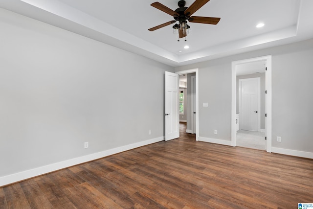 unfurnished bedroom featuring baseboards, ceiling fan, dark wood-style flooring, a tray ceiling, and recessed lighting