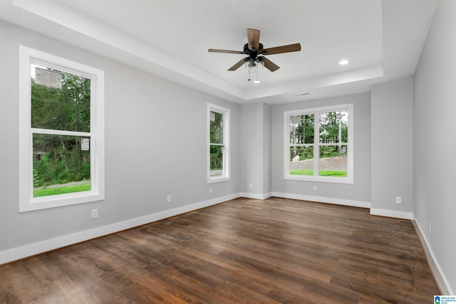 empty room with dark wood-type flooring, recessed lighting, a raised ceiling, and baseboards