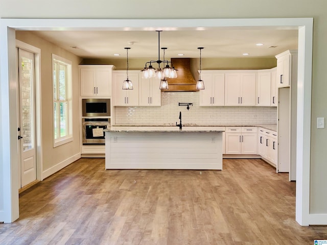 kitchen featuring light hardwood / wood-style flooring, light stone counters, premium range hood, hanging light fixtures, and white cabinets