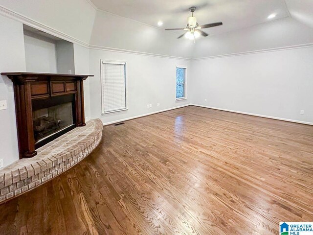 unfurnished living room with hardwood / wood-style floors, ceiling fan, a brick fireplace, and vaulted ceiling