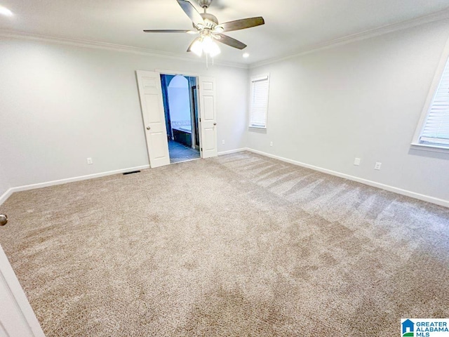 empty room with ceiling fan, a wealth of natural light, crown molding, and carpet floors