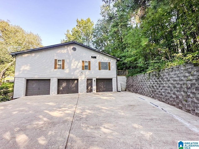 view of side of home featuring a garage, concrete driveway, brick siding, and fence