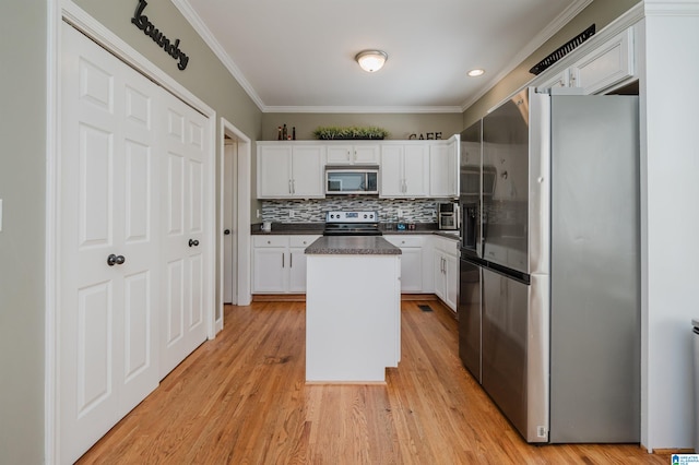 kitchen with ornamental molding, a kitchen island, appliances with stainless steel finishes, white cabinets, and light hardwood / wood-style flooring