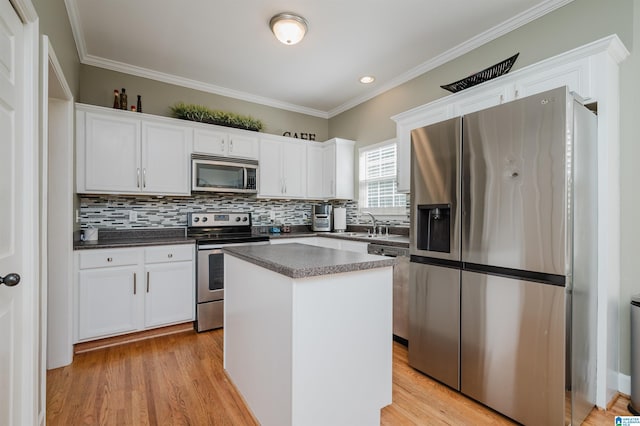 kitchen with dark countertops, a center island, crown molding, white cabinetry, and appliances with stainless steel finishes