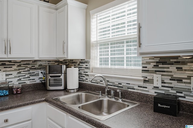 kitchen featuring white cabinets, dark countertops, backsplash, and a sink
