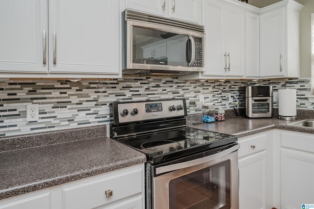 kitchen with dark countertops, backsplash, white cabinetry, and appliances with stainless steel finishes