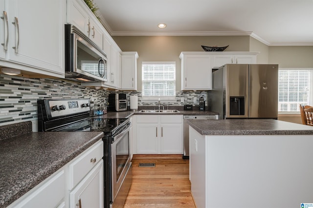 kitchen with dark countertops, appliances with stainless steel finishes, a sink, and white cabinets