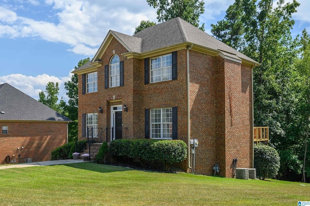 view of front of house with a front lawn, brick siding, central AC unit, and roof with shingles