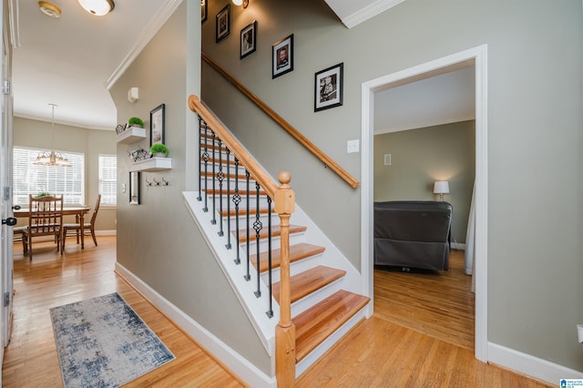 staircase with hardwood / wood-style flooring, a notable chandelier, and ornamental molding