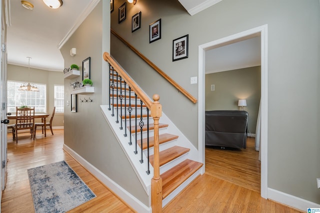 stairs with a notable chandelier, baseboards, crown molding, and wood finished floors