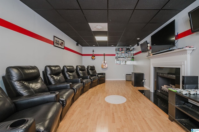 home theater room with a fireplace with flush hearth, baseboards, wood finished floors, and a drop ceiling
